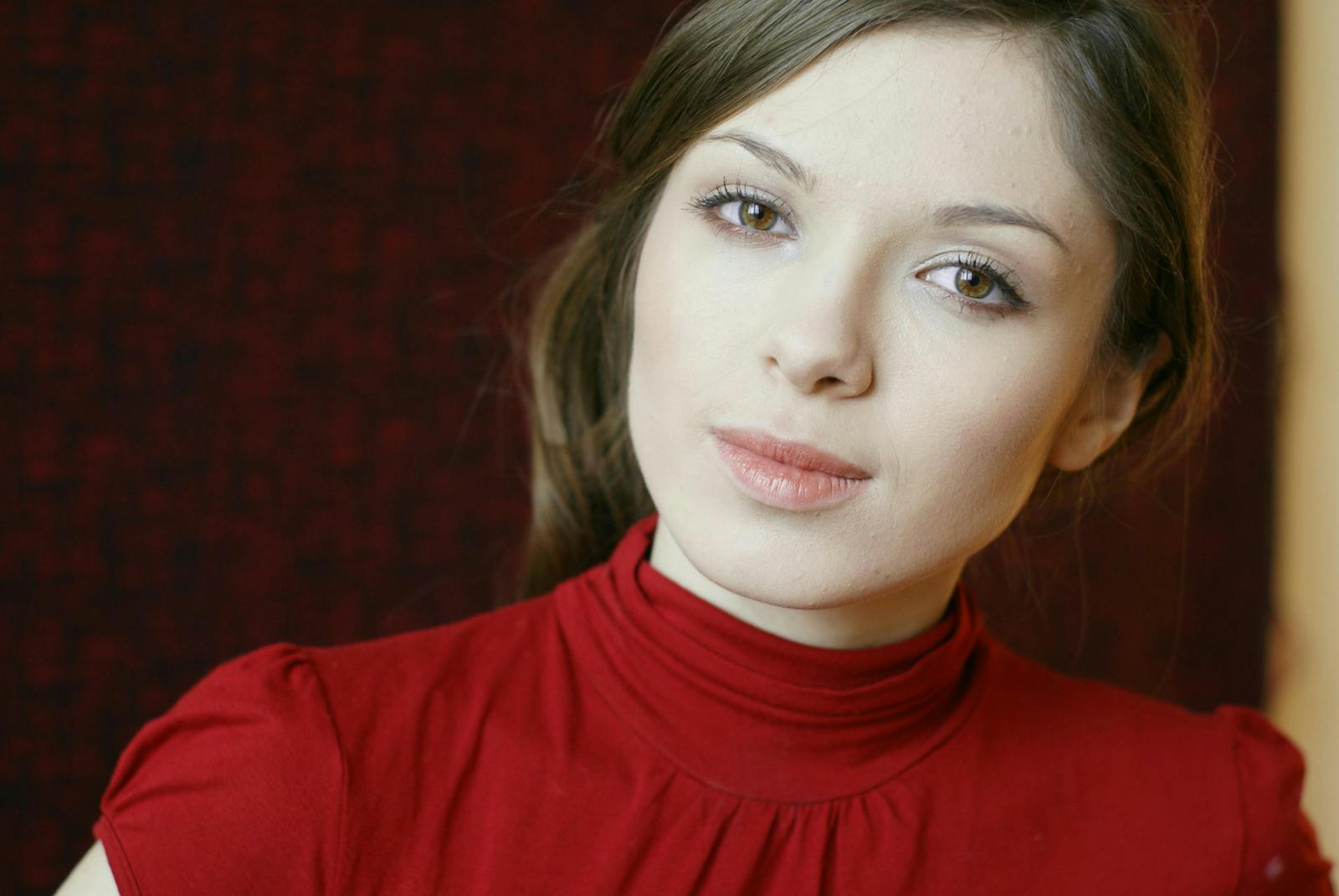 Close-up portrait of a woman wearing a red turtleneck with a neutral expression.