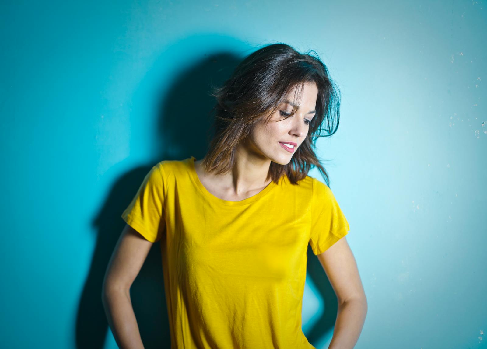 Portrait of a smiling woman in a yellow shirt against a blue wall.