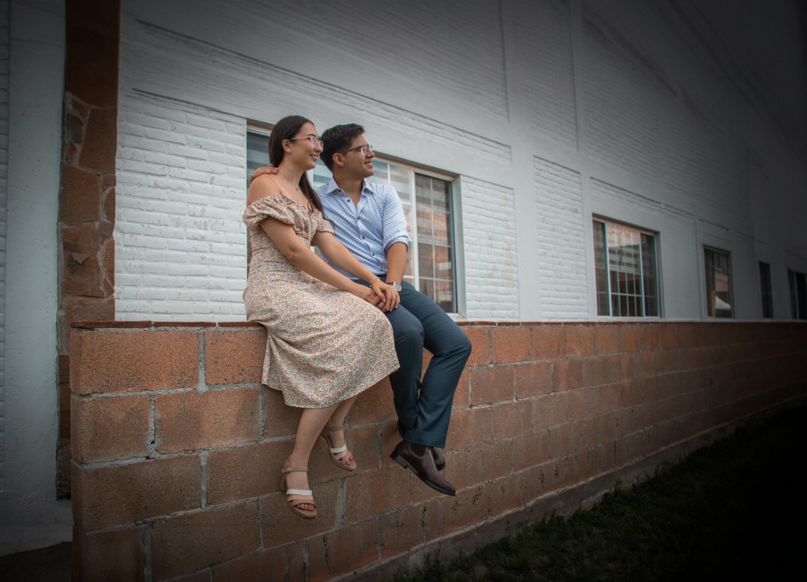 A man and a woman sitting on a brick wall