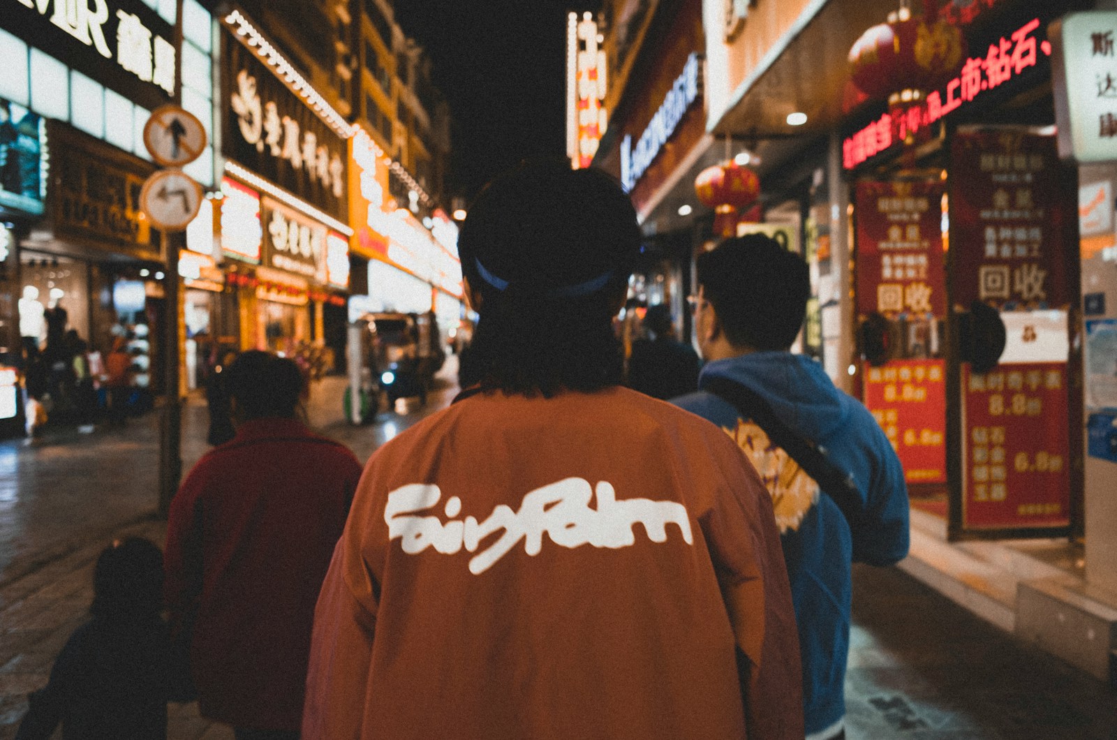 man in brown and white hoodie standing in front of people walking on street during nighttime